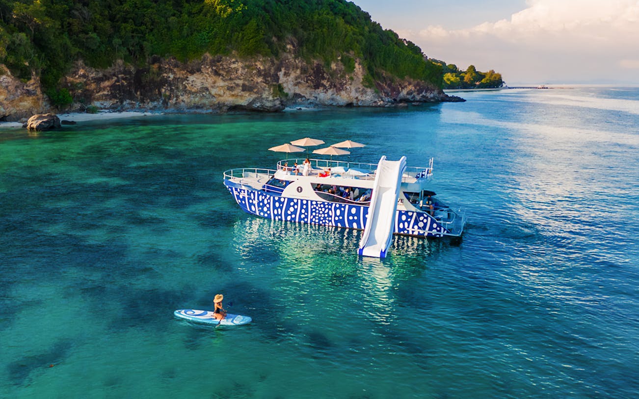 Tourist kayaking near whale shark fleet boat with slide in tropical waters.