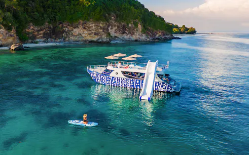 Tourist kayaking near whale shark fleet boat with slide in tropical waters.