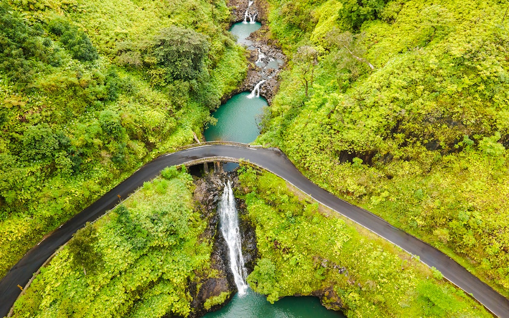 Aerial view of Maui waterfalls with lush greenery and winding road.