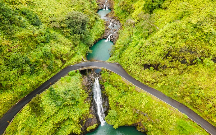 Aerial view of Maui waterfalls with lush greenery and winding road.