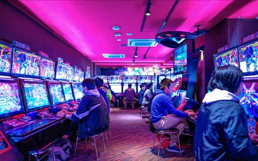 People playing arcade games in Akihabara gaming center during retro gaming tour.