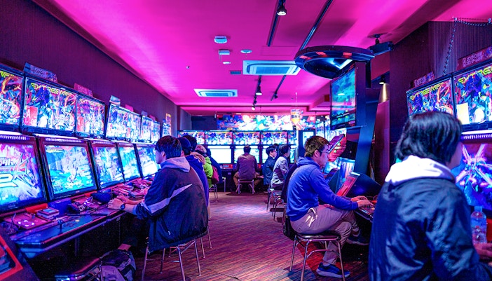 People playing arcade games in Akihabara gaming center during retro gaming tour.