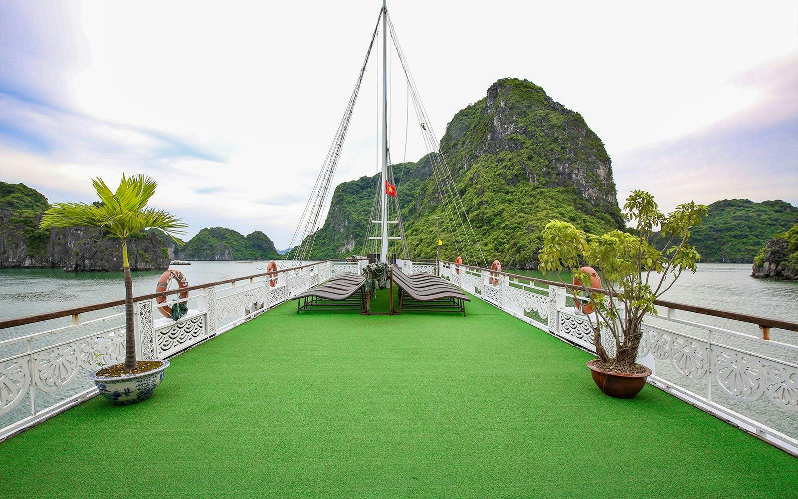 Cruise deck with lounge chairs and greenery, Halong Bay limestone cliffs in background.