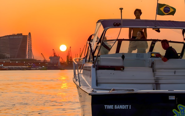 Tourists on a boat during Rio de Janeiro sunset cruise with city skyline and ferris wheel.