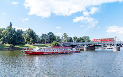Red sightseeing boat on Stockholm's waterway near a bridge and greenery.