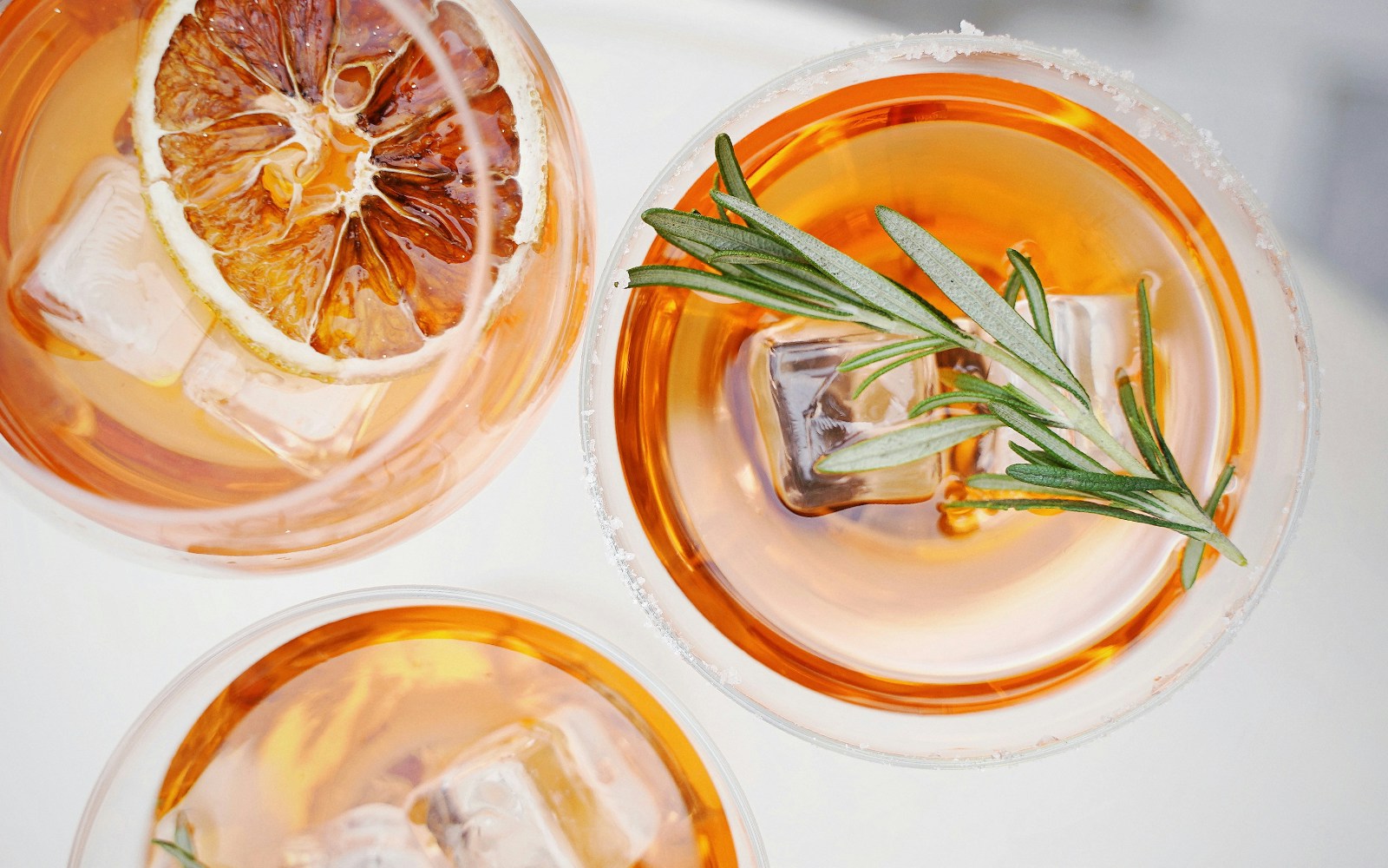 Cocktails with ice, citrus slice, and rosemary garnish at a bar.