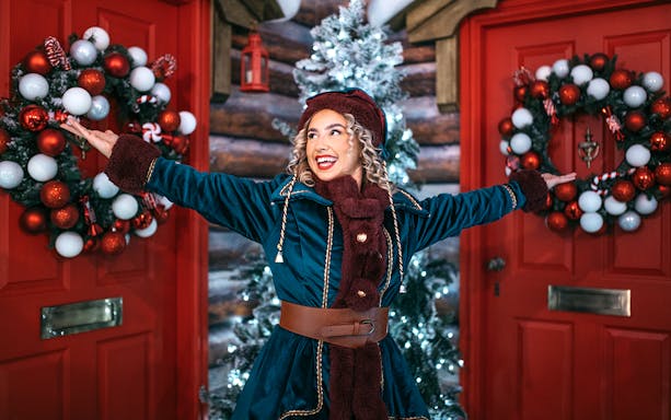 Elf in festive attire at Dubai Mall with holiday decorations.