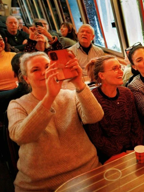 People enjoying a canal cruise during the Amsterdam Light Festival, capturing the view on their phones.