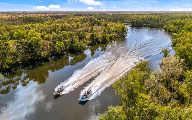 Airboats speeding along the Finniss River surrounded by lush greenery on the Top End Safari Camp tour.