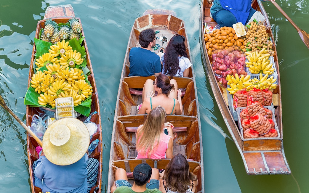 Boats with tourists and vendors selling fruit at Damnoen Saduak Floating Market, Thailand.