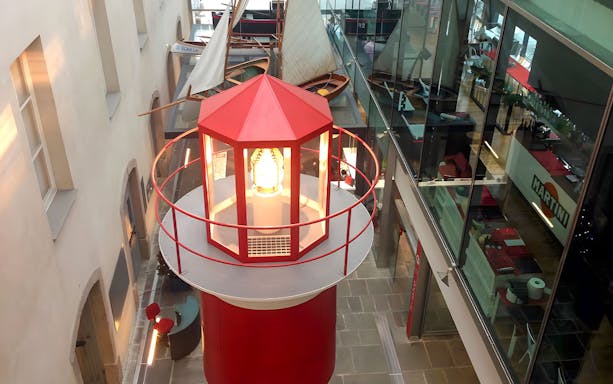 Lighthouse exhibit inside Galata Museo del Mare, Genoa, with sailboats displayed nearby.