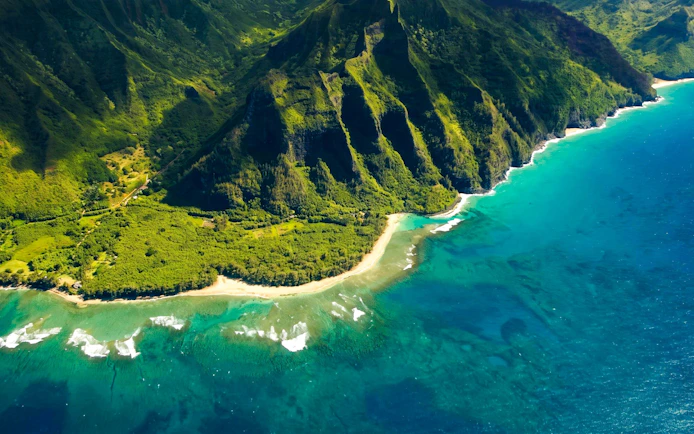 Aerial view of Kauai coastline with lush green cliffs and turquoise ocean.