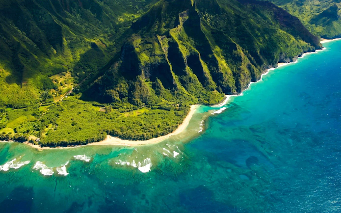 Aerial view of Kauai coastline with lush green cliffs and turquoise ocean.