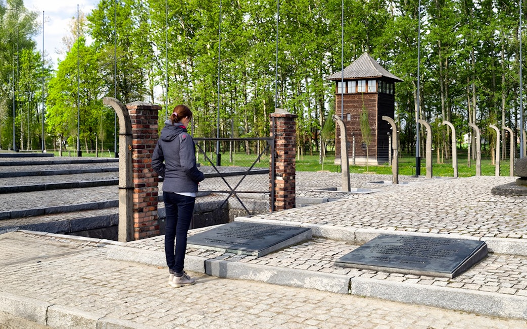 Visitor at Auschwitz Birkenau memorial site near watch tower and plaques.