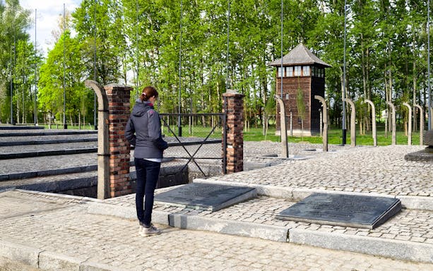 Visitor at Auschwitz Birkenau memorial site near watch tower and plaques.