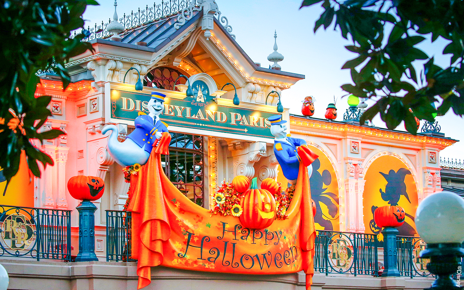 Disneyland Paris entrance decorated for Halloween with pumpkins and ghost figures.