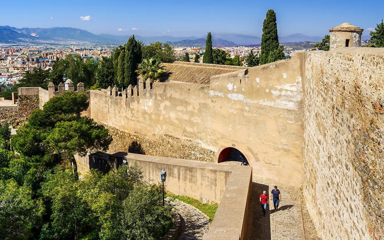 Gibralfaro Castle walls with tourists walking, overlooking Malaga cityscape.