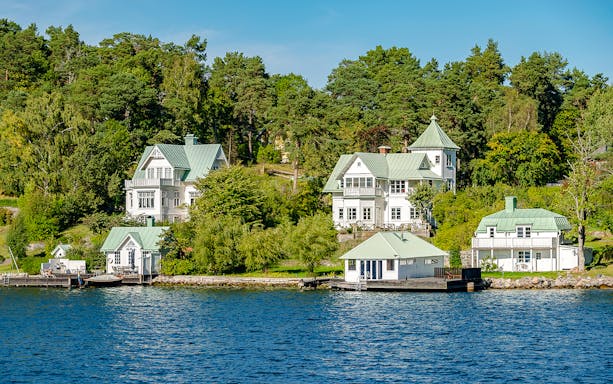 Stockholm waterfront houses with green roofs surrounded by trees and water.