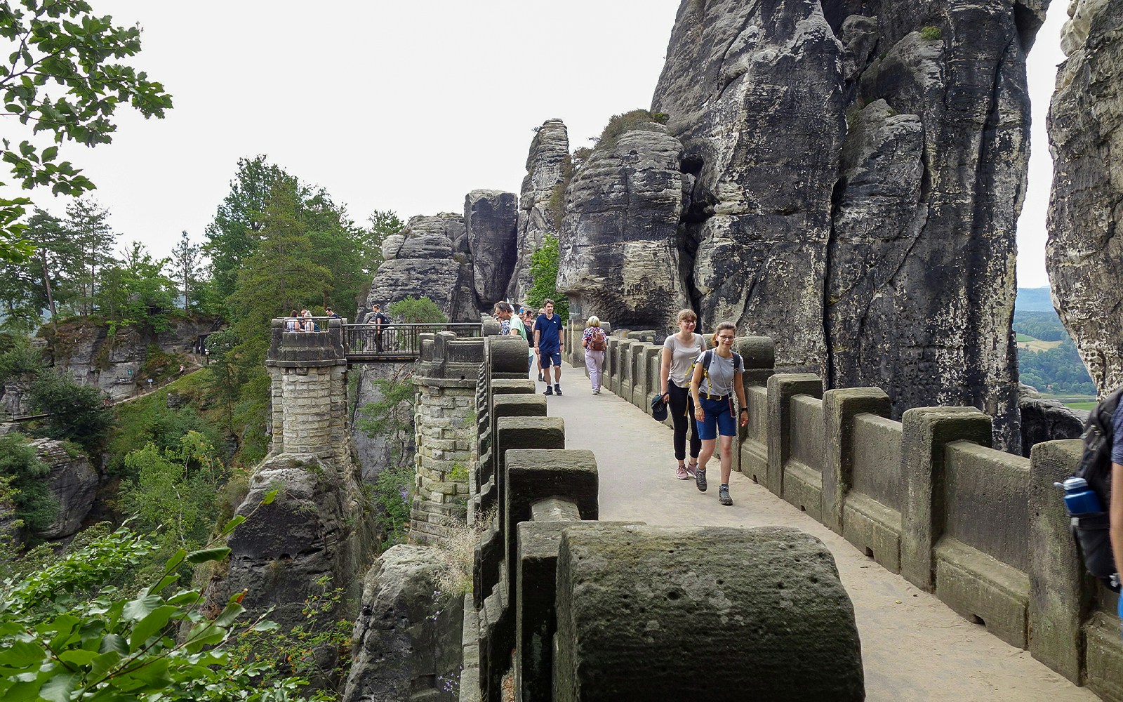 Visitors walking on Bastei Bridge in Saxon Switzerland, surrounded by rock formations.