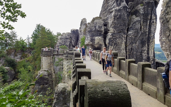Visitors walking on Bastei Bridge in Saxon Switzerland, surrounded by rock formations.