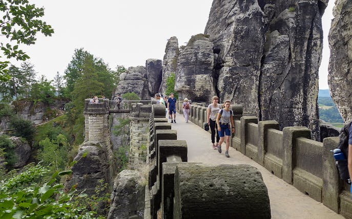 Visitors walking on Bastei Bridge in Saxon Switzerland, surrounded by rock formations.