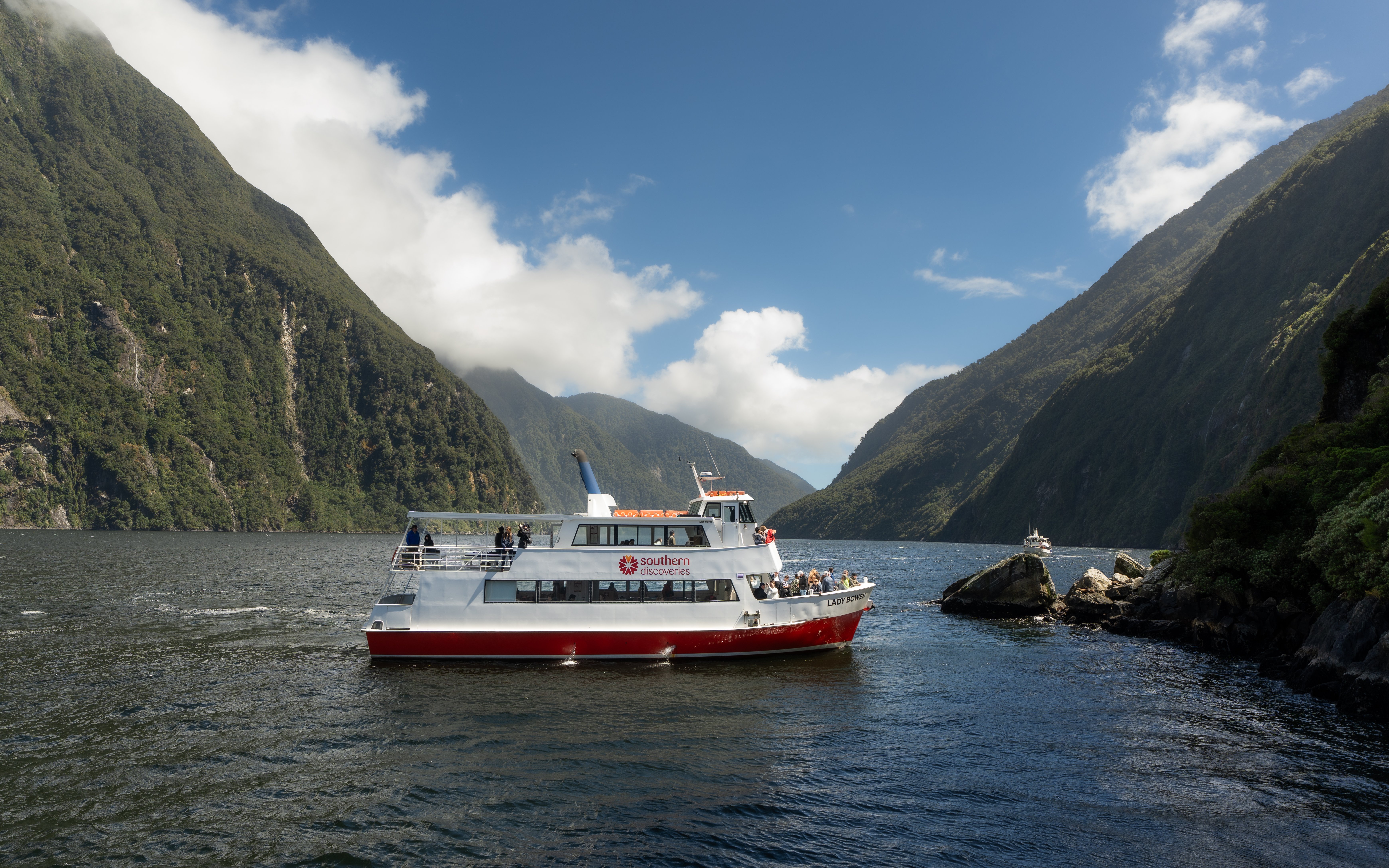 Cruise boat navigating Milford Sound fjord with lush cliffs in New Zealand.