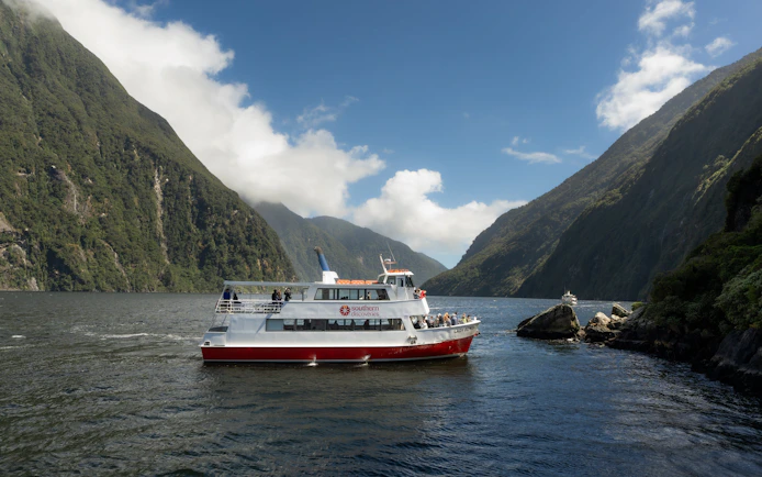 Cruise boat navigating Milford Sound fjord with lush cliffs in New Zealand.