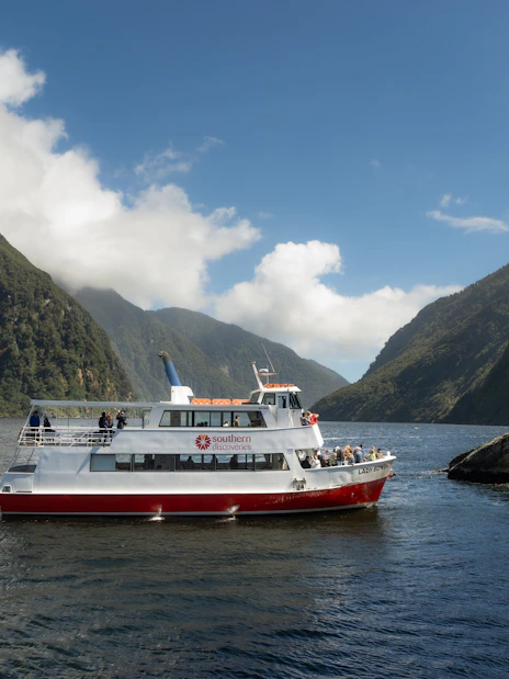 Cruise boat navigating Milford Sound fjord with lush cliffs in New Zealand.