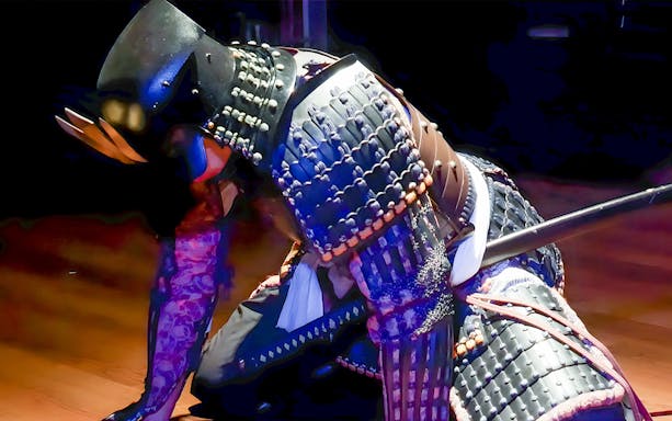 Samurai in armor performing sword trial cutting at Tokyo theater.