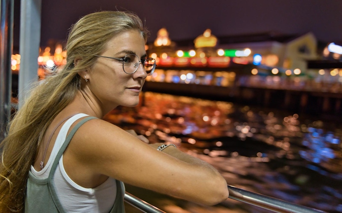 Person enjoying Vistula River night cruise with Krakow lights in background.