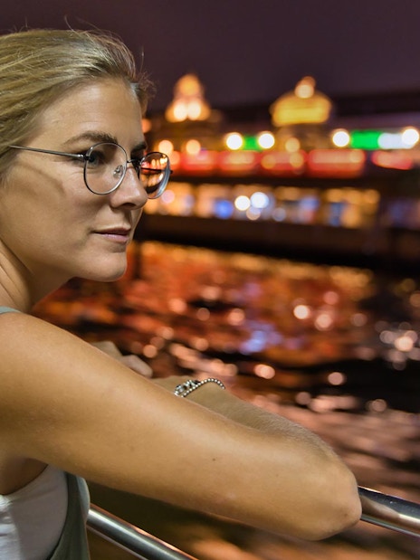 Person enjoying Vistula River night cruise with Krakow lights in background.