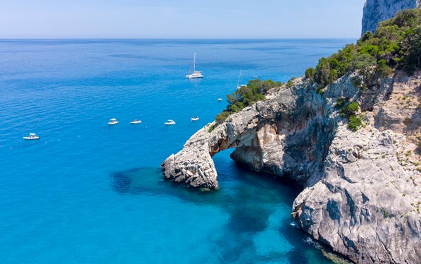 Boats near rocky arch along Baunei Coast during full-day guided tour.