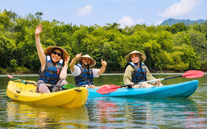 Tourists in conical hats kayaking on a river with lush green hills in the background.