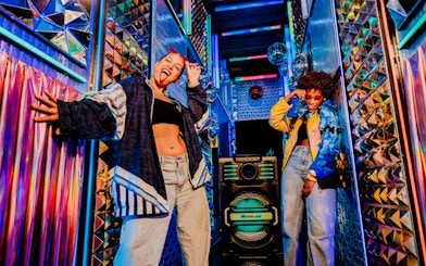 Visitors enjoying vibrant room at Upside Down Amsterdam with colorful lights and decor.