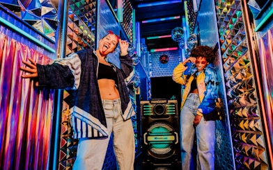 Visitors enjoying vibrant room at Upside Down Amsterdam with colorful lights and decor.