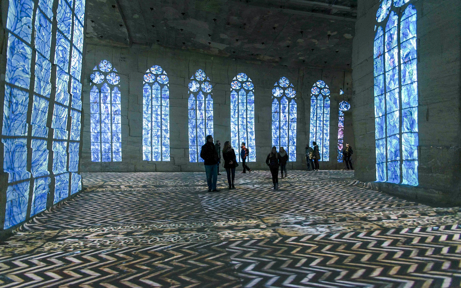 Visitors at Frieda Kahlo Exhibition in Carrières des Lumières, Paris, with projected art on walls.