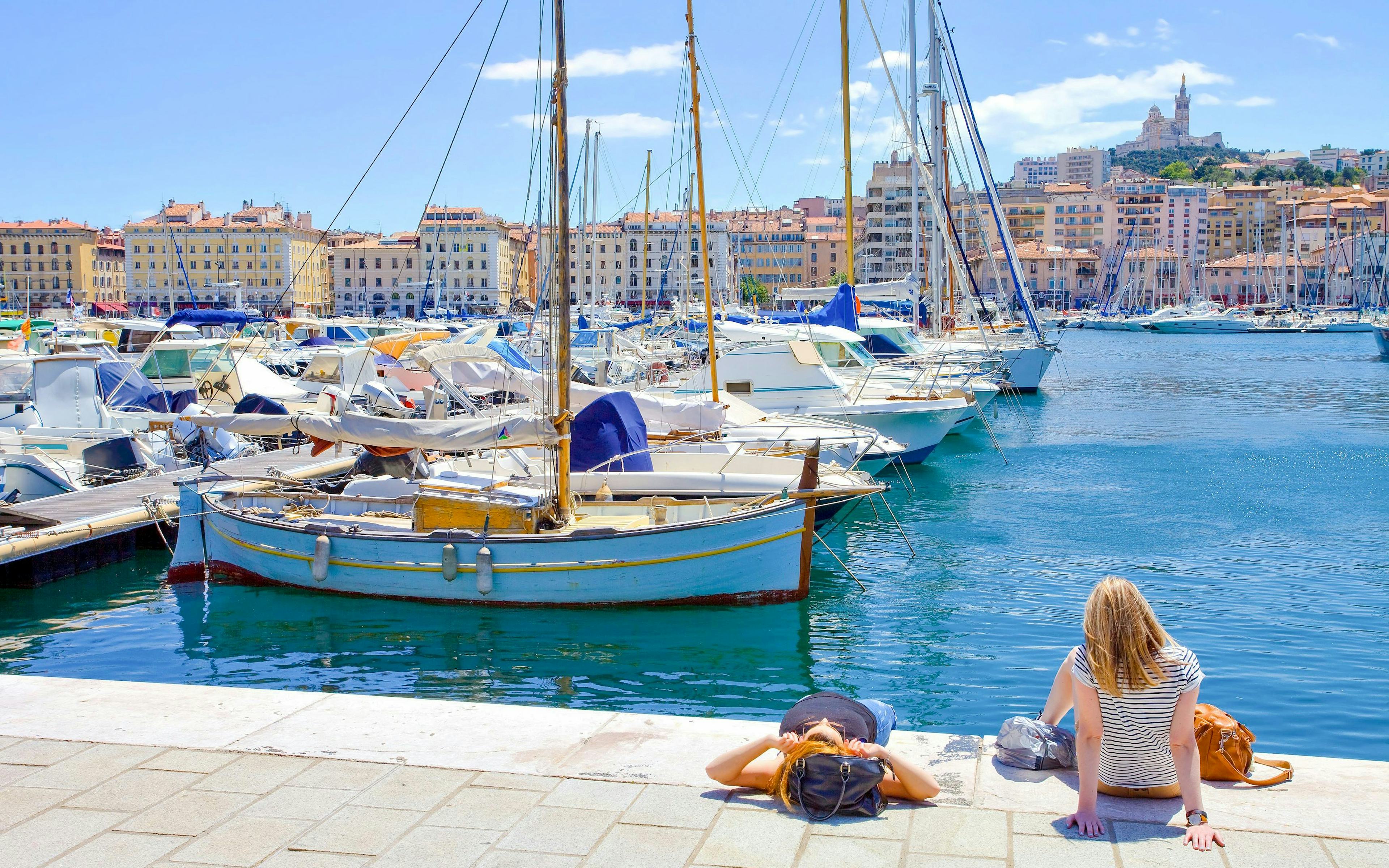 Boats docked at Marseille's Vieux Port with Notre-Dame de la Garde in the background.