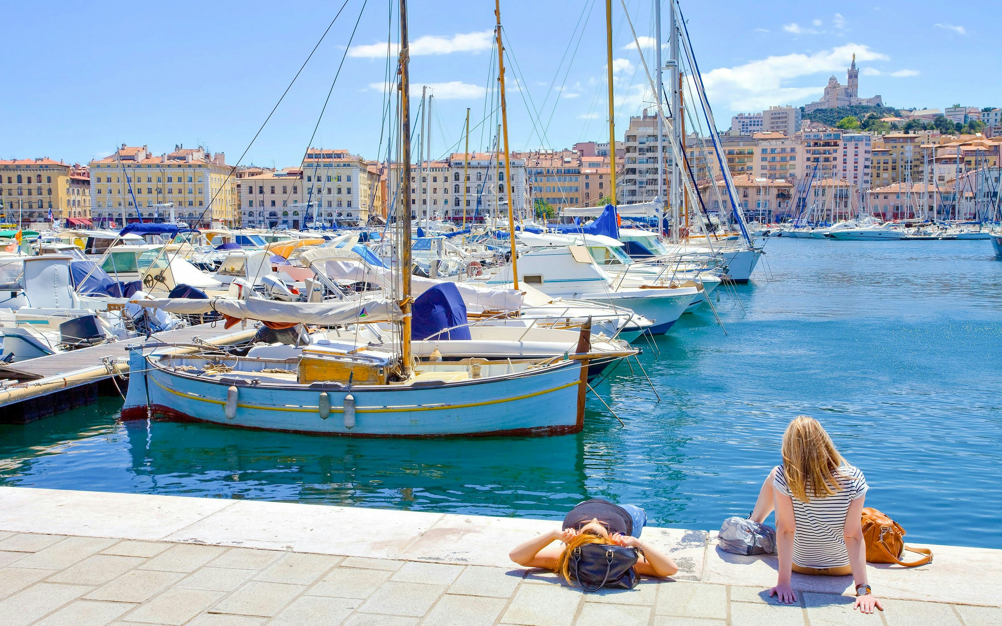 Boats docked at Marseille's Vieux Port with Notre-Dame de la Garde in the background.