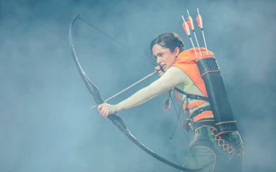 Performer with bow and arrows in Hunger Games West End show.