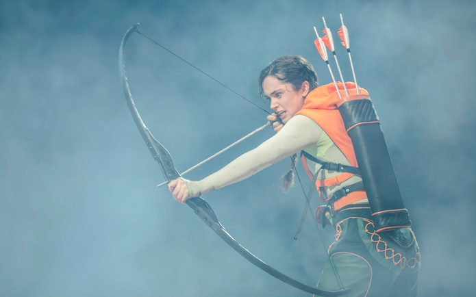 Performer with bow and arrows in Hunger Games West End show.