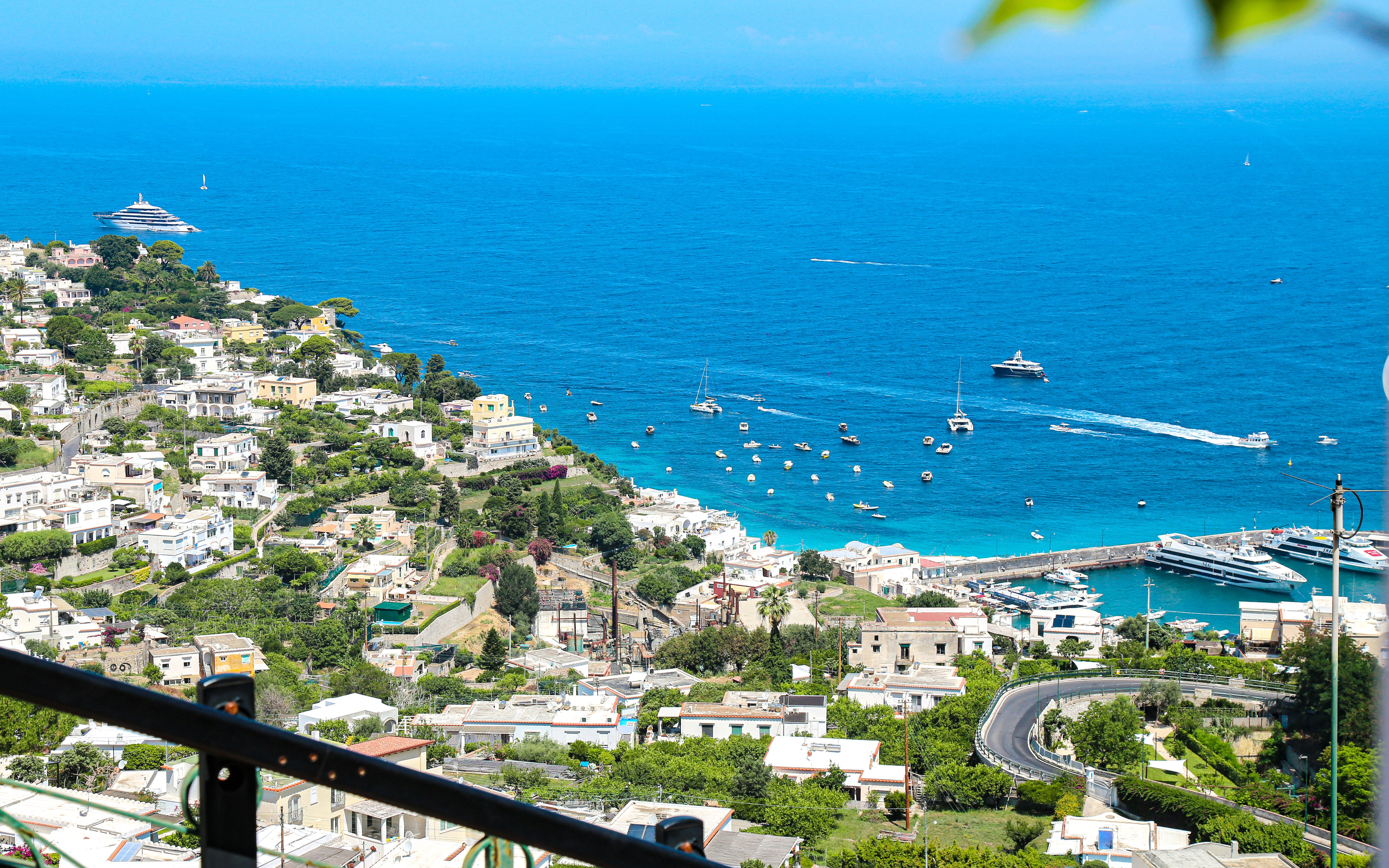 Coastline view from a terrace in Capri, Italy, overlooking the Tyrrhenian Sea with boats and villas.