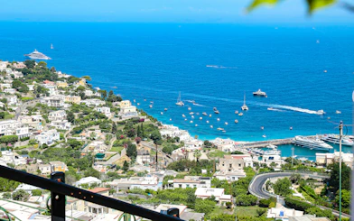 Coastline view from a terrace in Capri, Italy, overlooking the Tyrrhenian Sea with boats and villas.