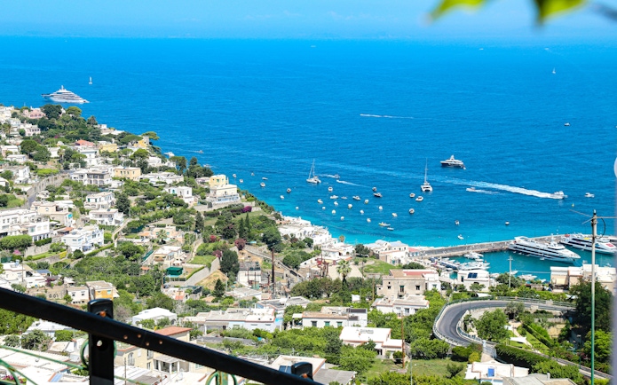 Coastline view from a terrace in Capri, Italy, overlooking the Tyrrhenian Sea with boats and villas.