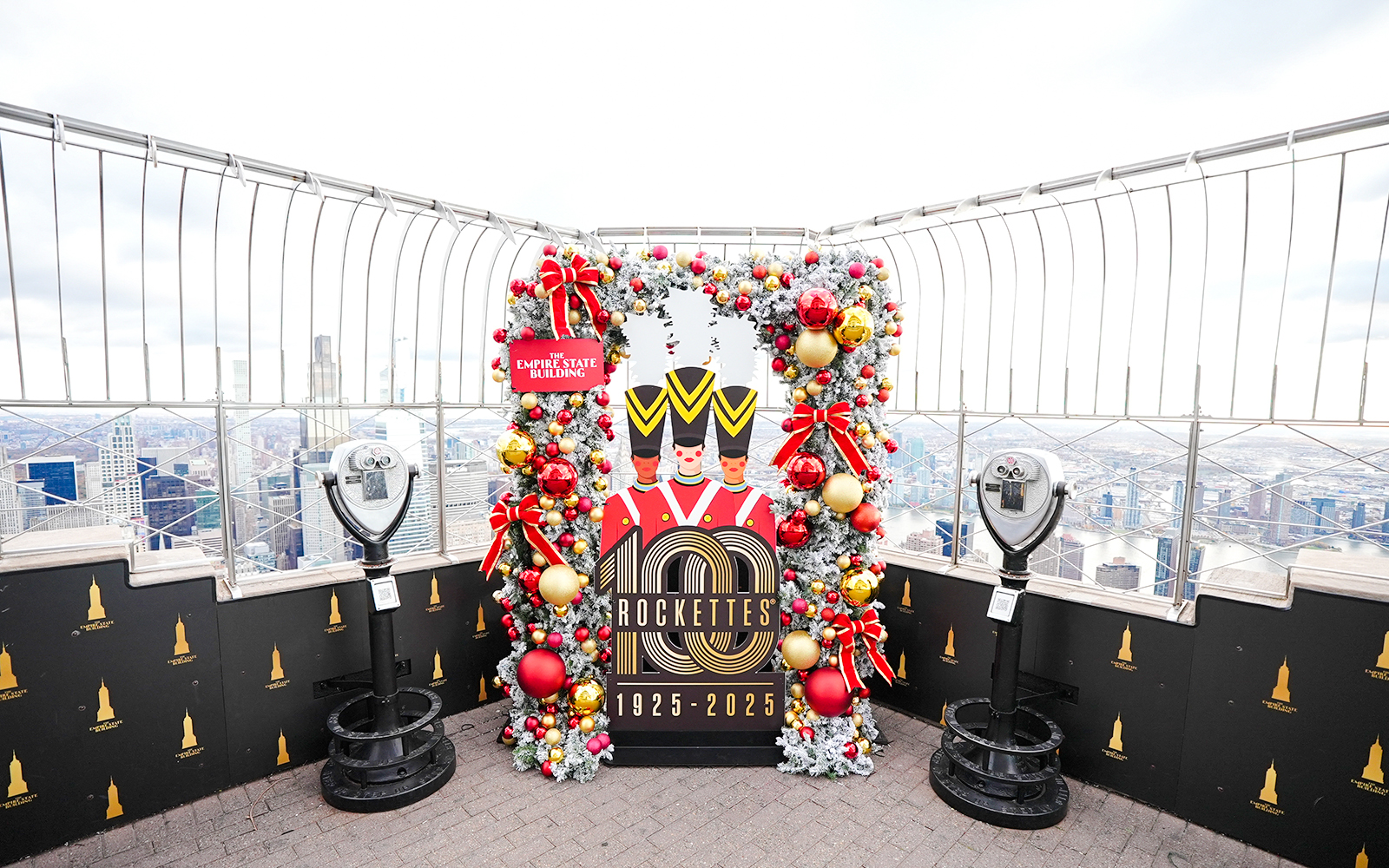 Empire State Building Christmas display with Rockettes sign and city view.