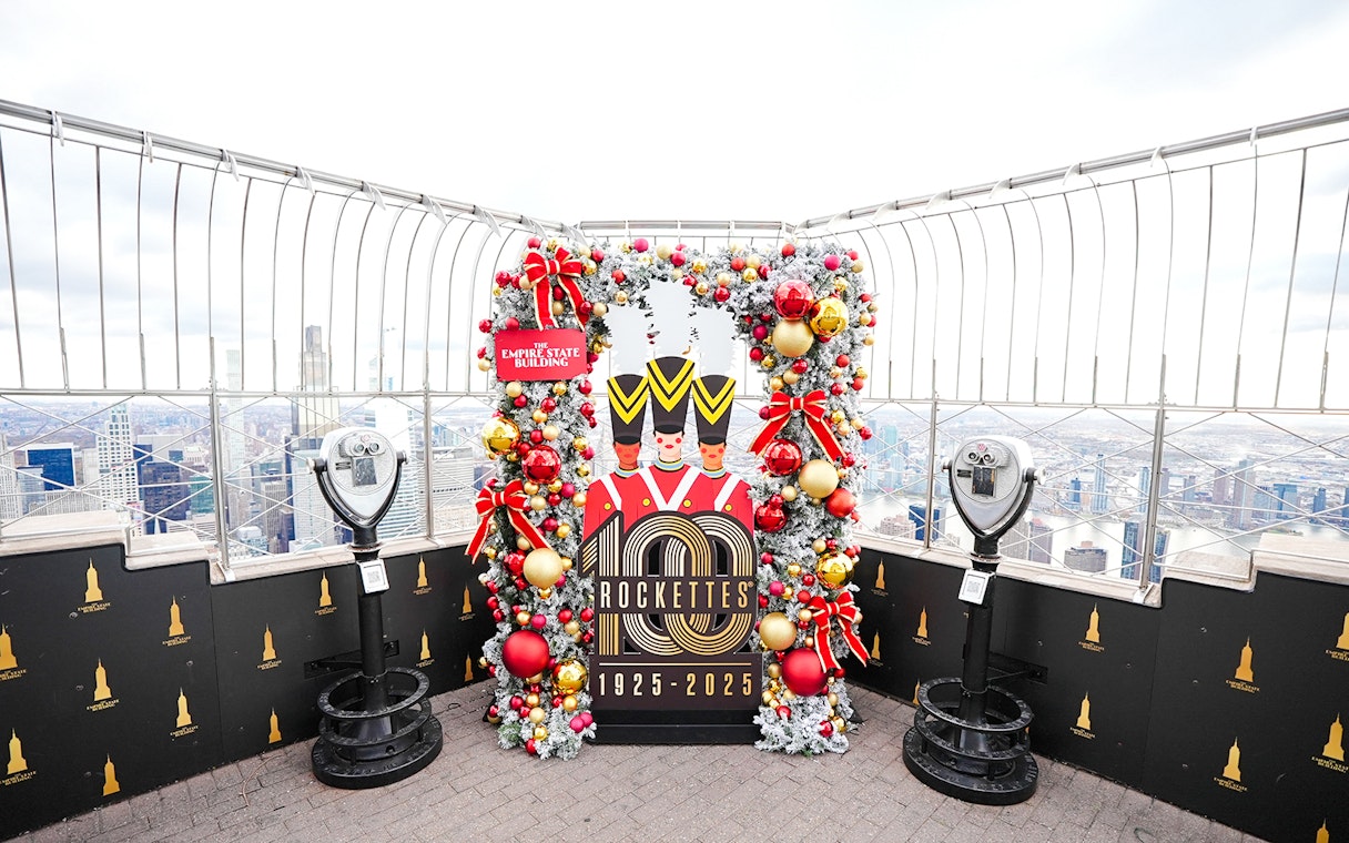 Empire State Building Christmas display with Rockettes sign and city view.