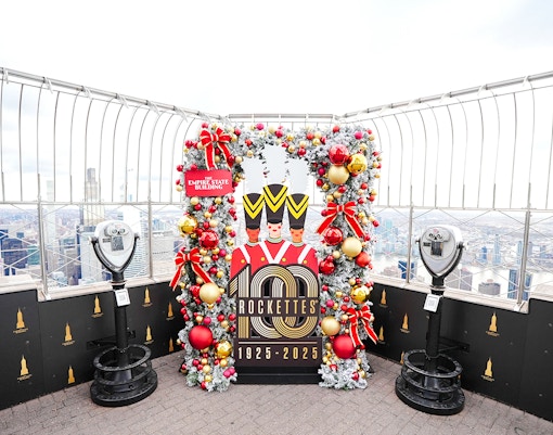 Empire State Building Christmas display with Rockettes sign and city view.