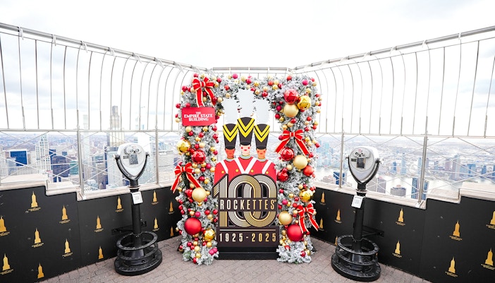 Empire State Building Christmas display with Rockettes sign and city view.