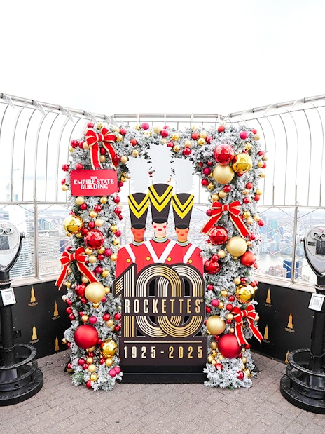 Empire State Building Christmas display with Rockettes sign and city view.
