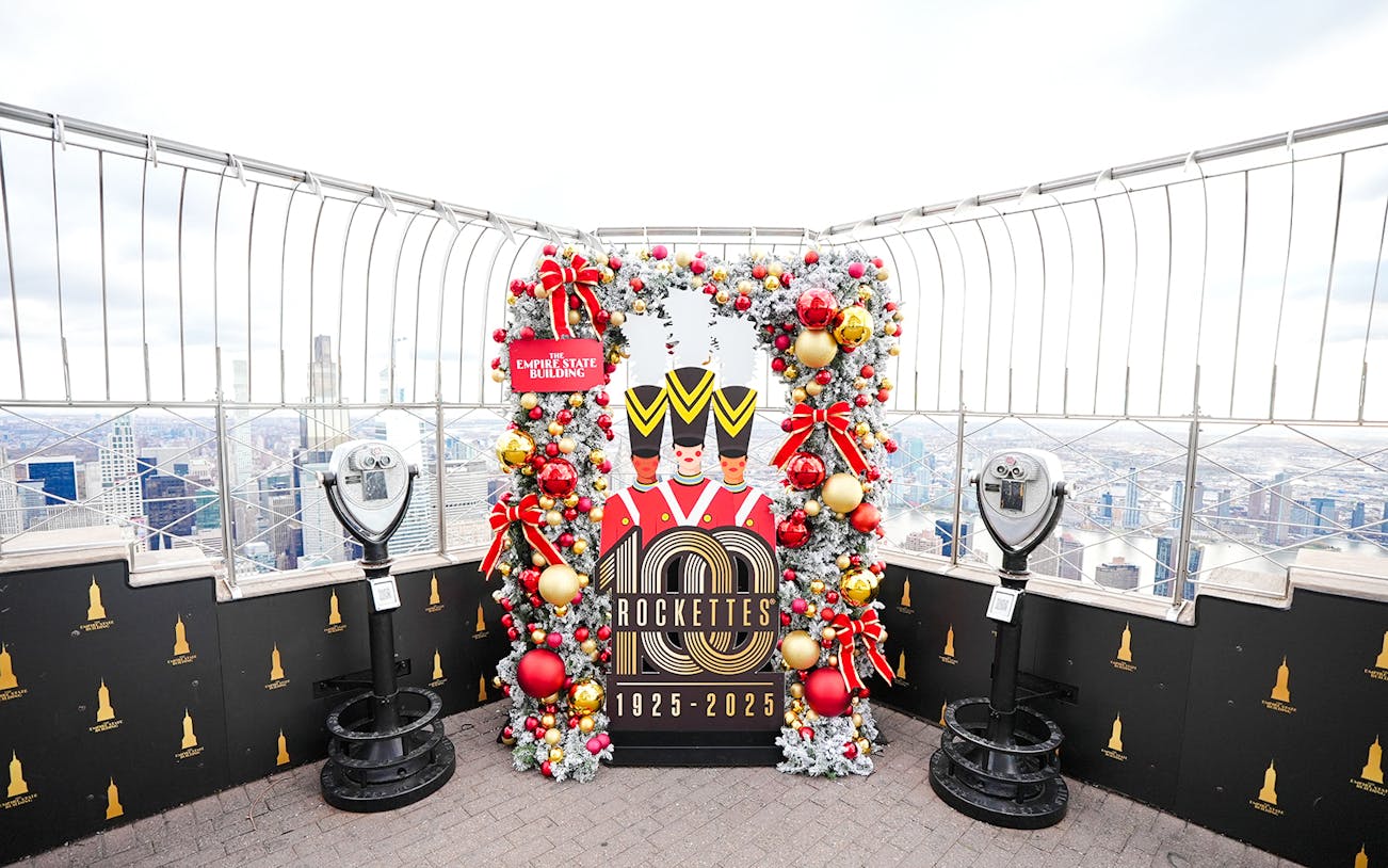 Empire State Building Christmas display with Rockettes sign and city view.