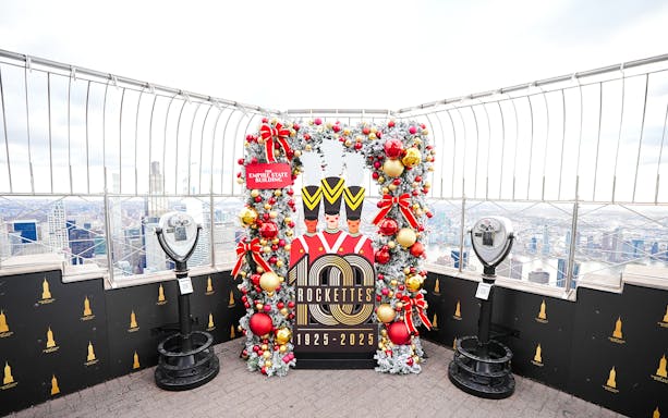 Empire State Building Christmas display with Rockettes sign and city view.